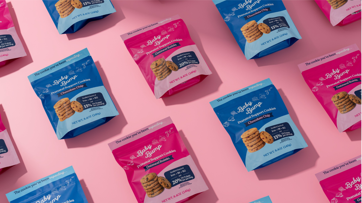 Multiple bags of Baby Bump Premium Flavored Cookies arranged in a repeating pattern on a solid pink background. The bags alternate between blue and pink packaging with white branding text.