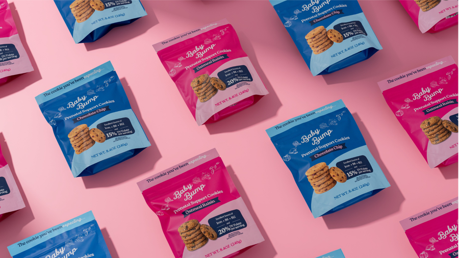 Multiple bags of Baby Bump Premium Flavored Cookies arranged in a repeating pattern on a solid pink background. The bags alternate between blue and pink packaging with white branding text.