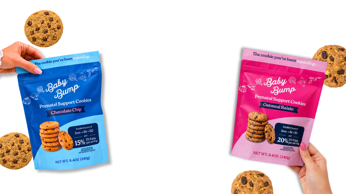 Two hands holding bags of Baby Bump Prenatal Support Cookies, with loose chocolate chip & oatmeal cookies scattered around. One bag is blue for Chocolate Chip cookies and the other is pink for Oatmeal Raisin cookies.